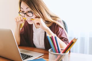 Designer looking at computer while chewing on colored pencil