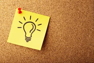 Sticky note pinned to a cork board with a drawing of a lightbulb